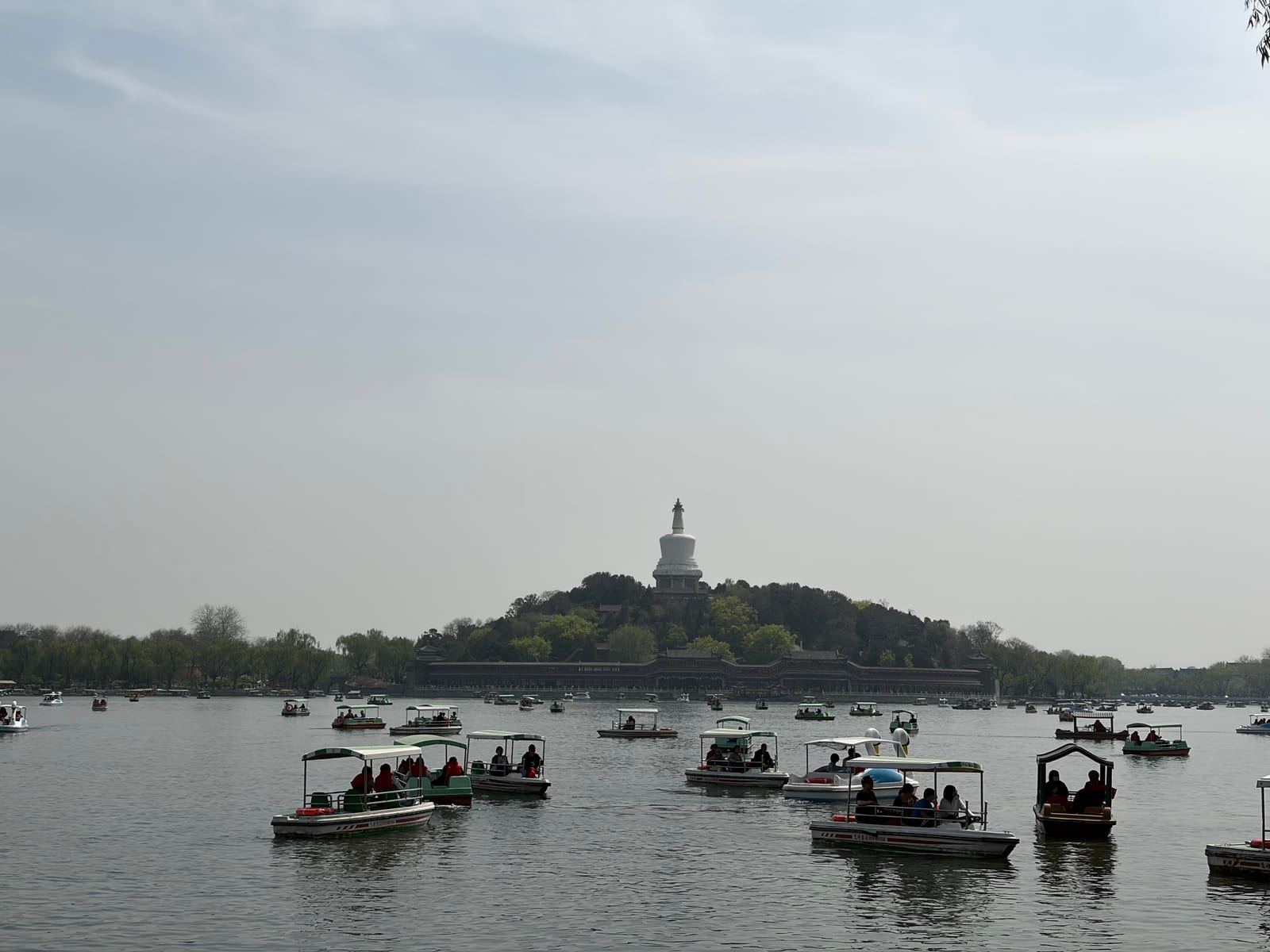 北海公园湖面上游船往来，远处白塔立在树影后的山上